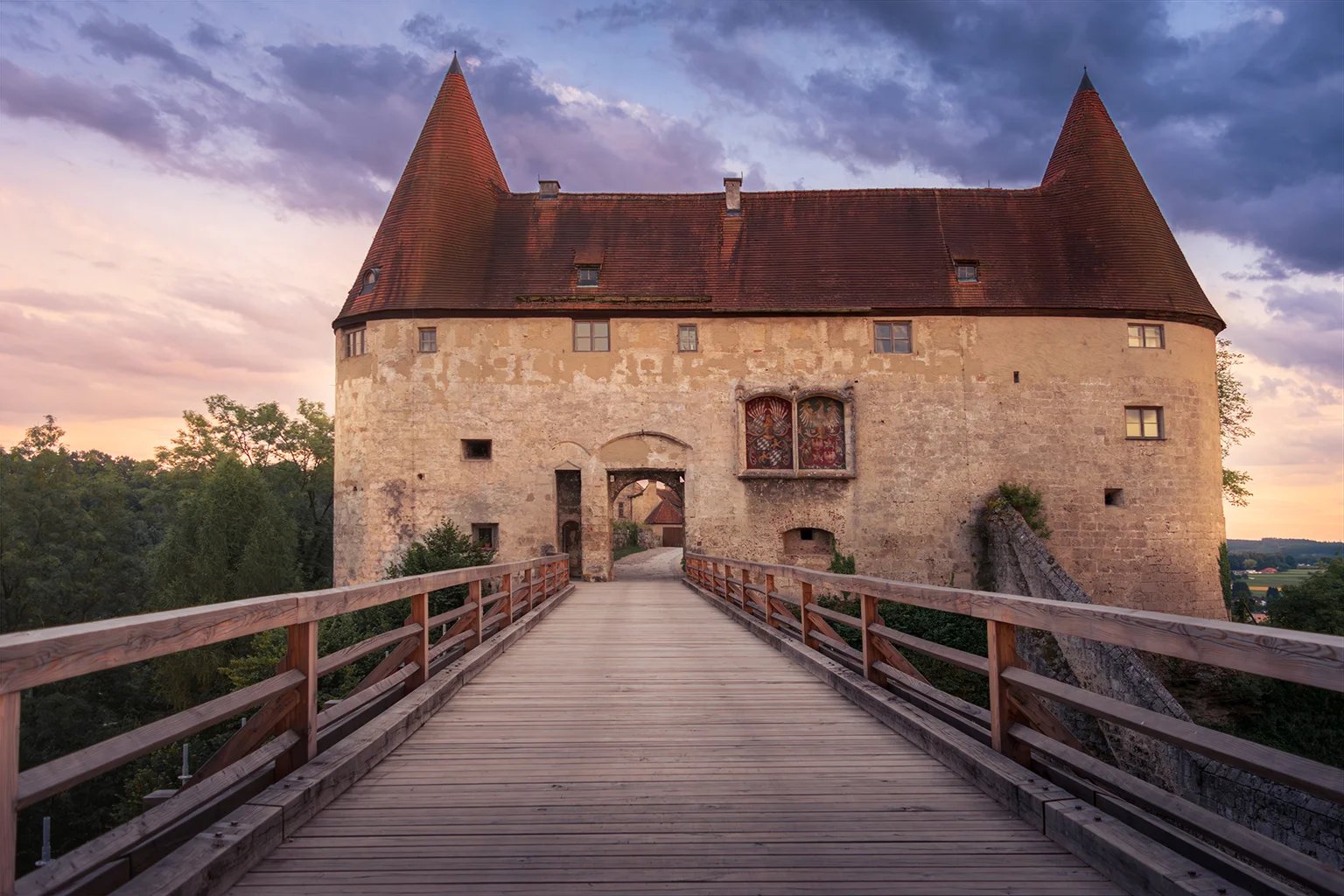 Ein Torhaus mit steilen Ziegeldächern, davor führt eine hölzerne Brücke über den Graben