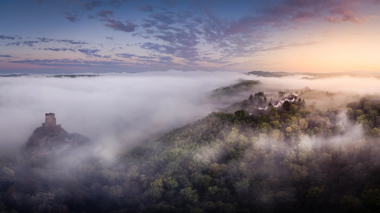Burgruinen ragen bei Sonnenaufgang aus einem Nebelmeer über bewaldeten Hängen