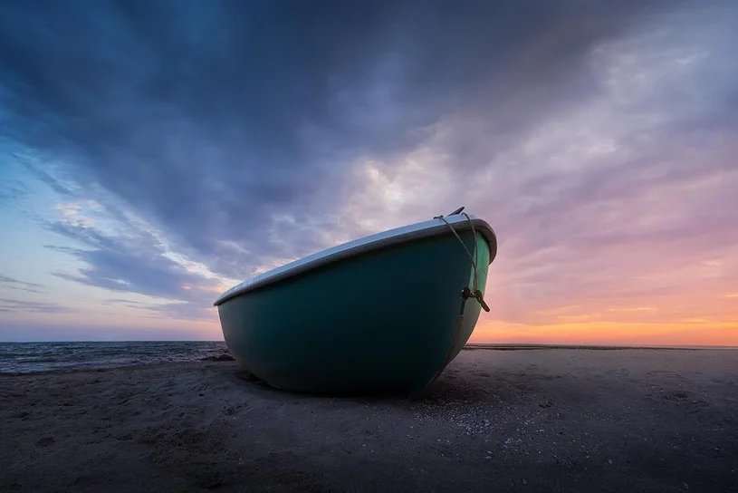 Ein Boot liegt bei Sonnenuntergang am Strand, darüber ziehen dunkle Wolken
